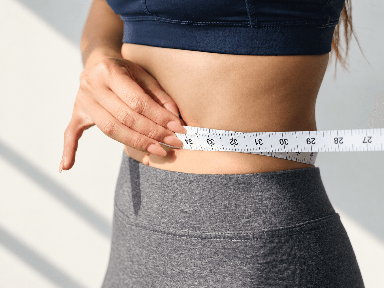 A tape measure held around a woman's waist over sports clothing