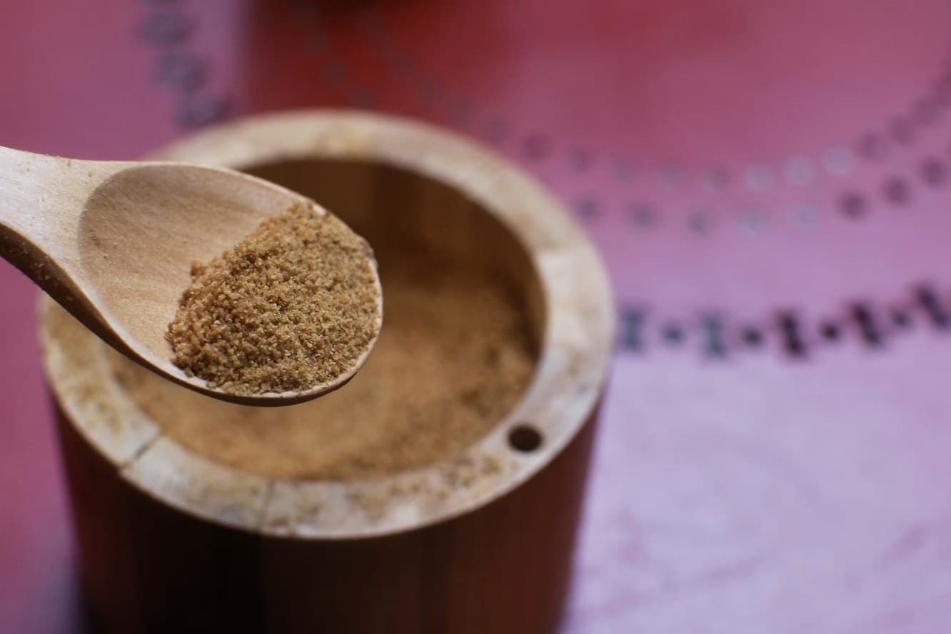 A wooden spoon of powdered Chinese herbs resting on a bamboo container.